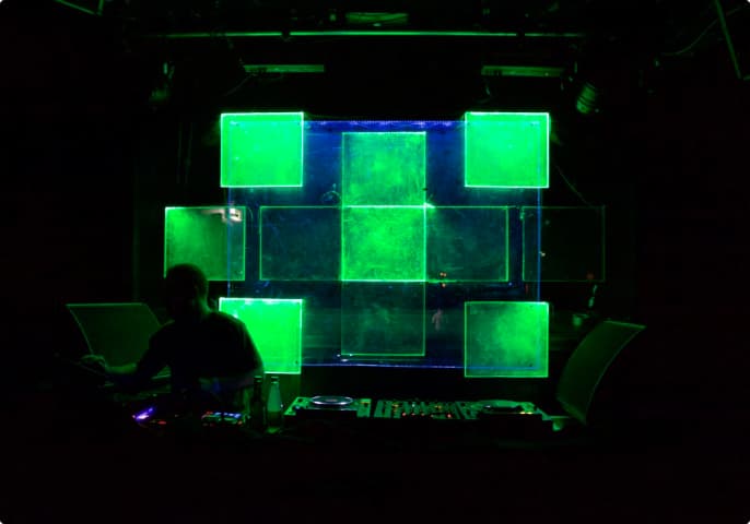 © James Morrison-Knight - Kultur For President 2019 - Acrylic glass installation 4 A DJ booth with square-shaped acrylic glass behind it that are glowing in green colors